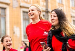 Three women in red shirts walking together, promoting a text to donate for a cause.